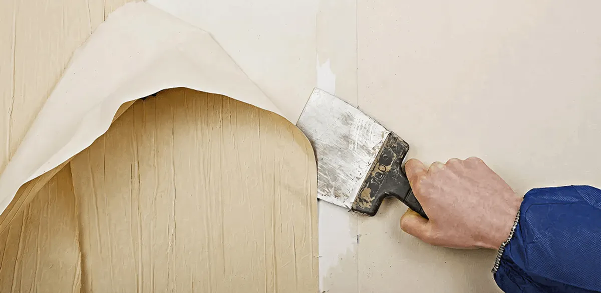 Handyman removing wallpaper with a scraper for wall preparation in New Orleans, LA